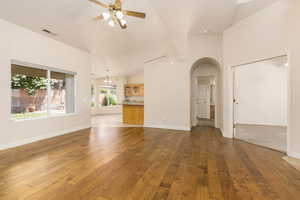 Unfurnished living room featuring ceiling fan, arched walkways, hardwood / wood-style flooring, and vaulted ceiling