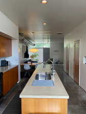 Kitchen featuring a sink, concrete countertops, natural lighting, wood cabinetry, and an island with sink