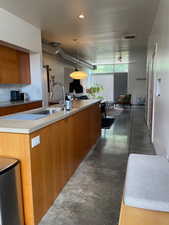 Kitchen featuring finished concrete flooring, modern wood cabinets, concrete countertops, and hanging light fixtures