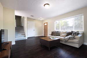 Living room featuring dark wood-type flooring, baseboards, stairway, and a textured ceiling