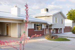 View of front of property with a chimney, brick siding, driveway, and metal roof