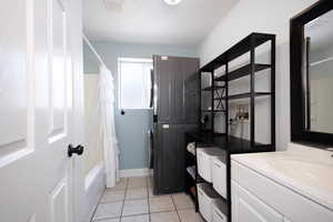 Bathroom with stacked washer / dryer, vanity, shower / bathtub combination with curtain, tile patterned flooring, and baseboards