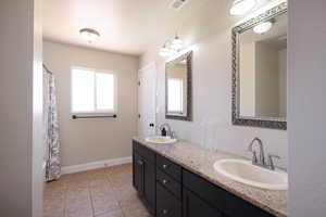Full bath featuring double vanity, tile patterned flooring, and baseboards