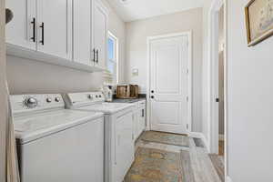 Washroom with washing machine and dryer, cabinet space, light wood-type flooring, and baseboards