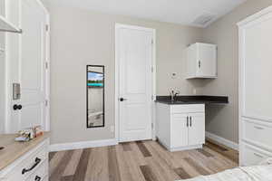 Kitchen featuring light wood-type flooring, white cabinetry, a sink, and baseboards