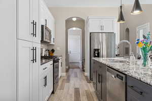 Kitchen featuring appliances with stainless steel finishes, light wood-type flooring, a sink, and white cabinetry