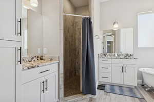Full bath with a tile shower, two vanities, wood finished floors, and a freestanding bath
