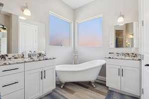 Full bath with wood finished floors, two vanities, a freestanding tub, and a stall shower