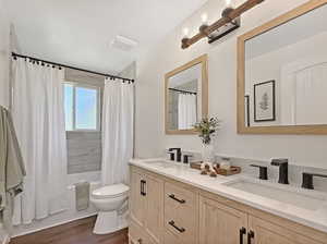 Bathroom featuring double vanity, shower / tub combo with curtain, toilet, and wood finished floors