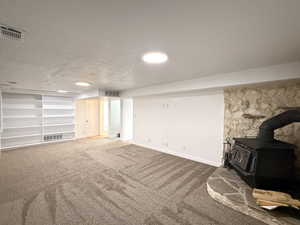 Unfurnished living room featuring a wood stove, carpet flooring, and baseboards