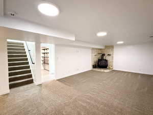 Unfurnished living room featuring carpet, a wood stove, stairway, and baseboards