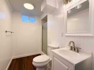 Bathroom featuring a shower with door, wood finished floors, toilet, vanity, and ornamental molding
