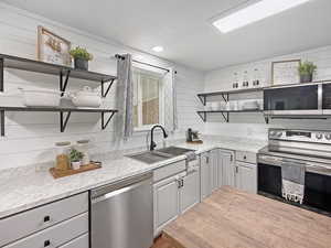 Kitchen with open shelves, appliances with stainless steel finishes, a sink, gray cabinetry, and a textured ceiling
