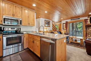 Kitchen featuring stainless steel appliances, a sink, wooden ceiling, a peninsula, and light stone counters