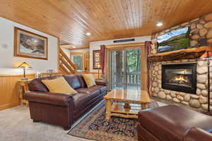 Living area featuring wood ceiling, wainscoting, a stone fireplace, stairs, and light carpet
