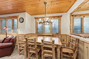 Carpeted dining space featuring wood ceiling, a wainscoted wall, healthy amount of natural light, wooden walls, and a chandelier