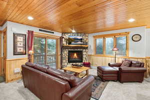Carpeted living room featuring wood walls, a wainscoted wall, wood ceiling, a stone fireplace, and baseboard heating