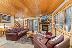 Carpeted living area featuring a wainscoted wall, wood walls, wooden ceiling, a fireplace, and stairway