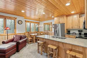 Kitchen with wood ceiling, wainscoting, wood walls, light stone countertops, and light brown cabinetry