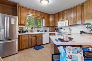 Kitchen featuring white appliances, light countertops, brown cabinets, light wood-style floors, and a sink