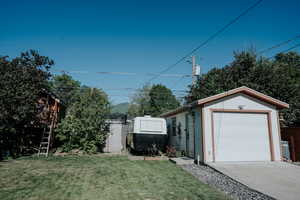 View of green lawn with an outdoor structure, a garage, and concrete driveway