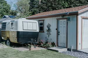 View of exterior entry with roof with shingles and a yard
