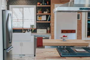Kitchen featuring appliances with stainless steel finishes, exhaust hood, white cabinets, a sink, and light countertops
