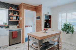 Kitchen featuring appliances with stainless steel finishes, plenty of natural light, light marble finish flooring, and open shelves