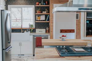 Kitchen with stainless steel appliances, a sink, white cabinetry, exhaust hood, and light countertops