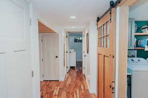 Hall with washer / clothes dryer, a barn door, and light wood-style floors
