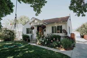 Bungalow-style home featuring a front yard, an outdoor structure, and a shingled roof