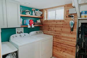 Washroom with independent washer and dryer, wooden walls, and cabinet space