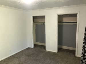 Unfurnished bedroom with multiple closets, dark carpet, ornamental molding, and baseboards