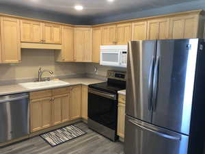 Kitchen featuring stainless steel appliances, a sink, wood finished floors, light countertops, and light brown cabinetry