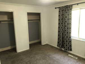 Unfurnished bedroom with dark carpet, two closets, ornamental molding, and baseboards