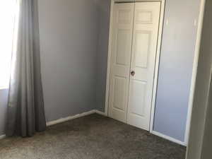 Unfurnished bedroom with dark carpet, baseboards, and a closet