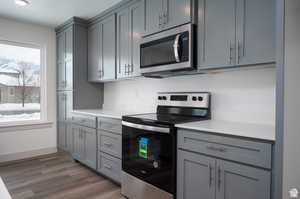 Kitchen with stainless steel appliances, gray cabinetry, light countertops, dark wood finished floors, and baseboards
