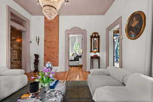 Living area featuring a chandelier, light wood-style floors, brick wall, and crown molding