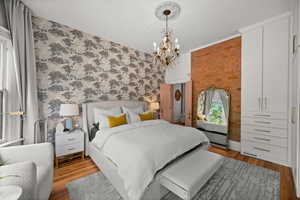 Bedroom with light wood finished floors, a chandelier, wallpapered walls, and brick wall