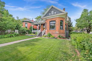 View of front of property with covered porch, a chimney, brick siding, and a front lawn