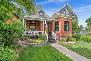 View of front of house featuring brick siding, a front lawn, a porch, a shingled roof, and a chimney