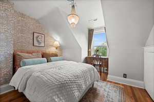Bedroom featuring baseboards, wood finished floors, wallpapered walls, and lofted ceiling