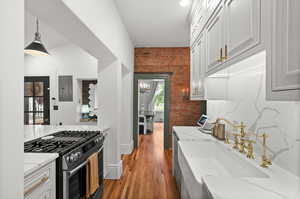 Kitchen featuring stainless steel range with gas cooktop, brick wall, light stone counters, electric panel, and a sink