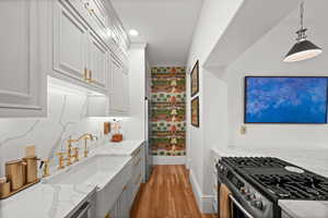 Kitchen with stainless steel gas range oven, baseboards, light wood-type flooring, light stone countertops, and hanging light fixtures