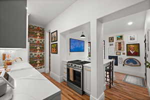 Kitchen featuring stainless steel gas stove, light wood finished floors, baseboards, light stone counters, and a breakfast bar