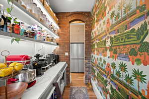 Kitchen featuring stainless steel refrigerator, brick wall, light wood finished floors, and light stone counters