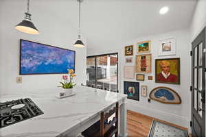 Kitchen featuring wood finished floors, light stone counters, lofted ceiling, pendant lighting, and baseboards