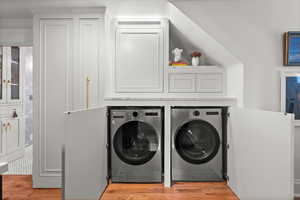 Laundry area with independent washer and dryer and light wood-style flooring