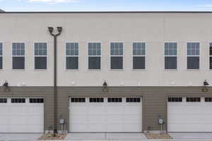 Rear view of house with stucco siding, an attached garage, and driveway