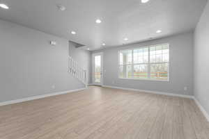 Unfurnished living room with light wood-style floors, stairs, recessed lighting, baseboards, and a textured ceiling